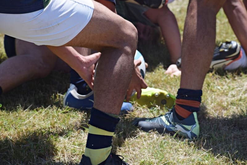 Piernas de varios jugadores y una mano agarrando el balón de rugby a ras de suelo
